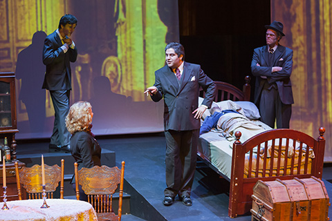 Four vocalists on stage perform a scene from an opera