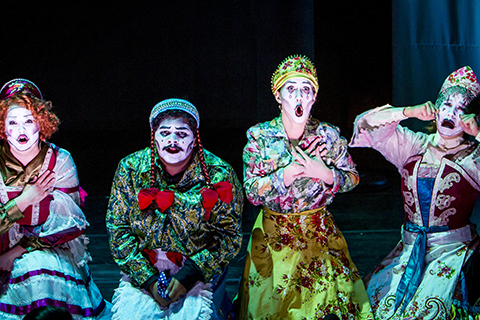 Actors with bright clothing and expressive makeup sign during an opera performance